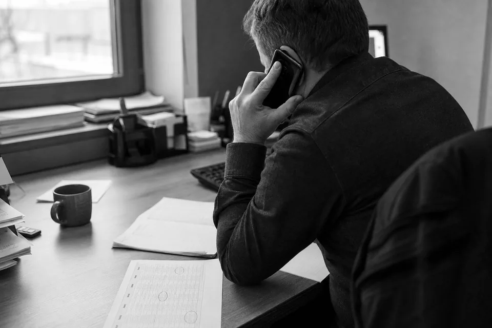 Handlowiec rozmawia przez telefon z klientem, przed nim lista firm i kalendarz